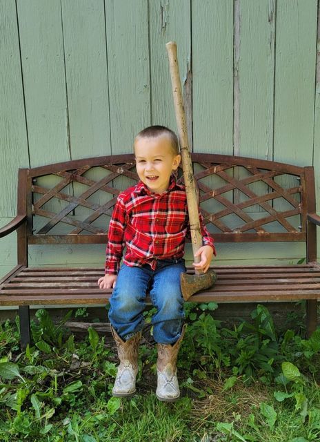 A little boy is sitting on a bench holding a bat.