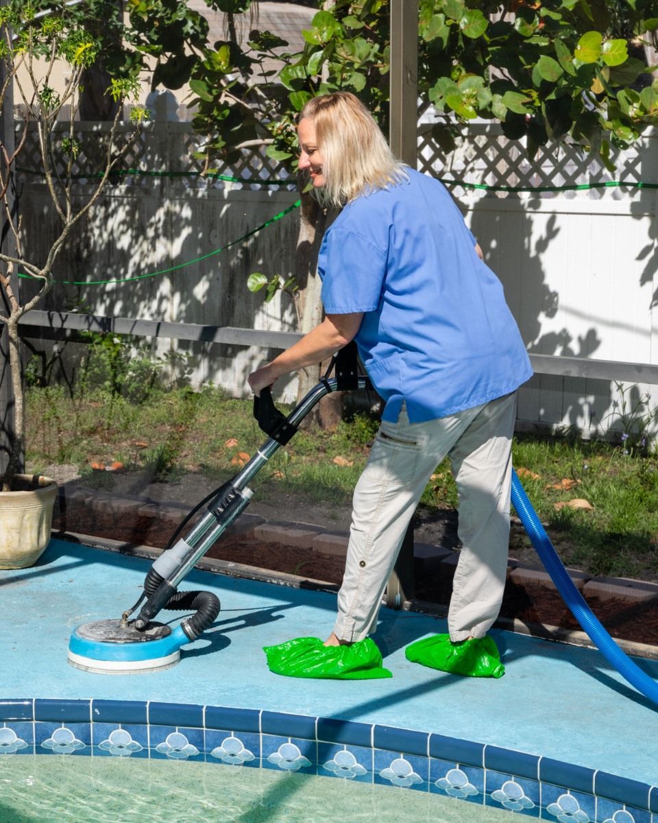 A woman is cleaning a swimming pool with a vacuum cleaner.