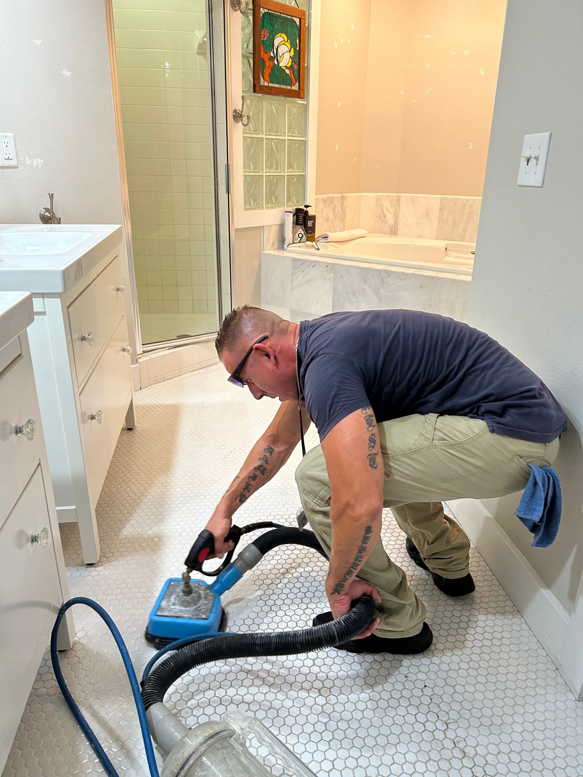 A man is kneeling down in a bathroom using a vacuum cleaner.