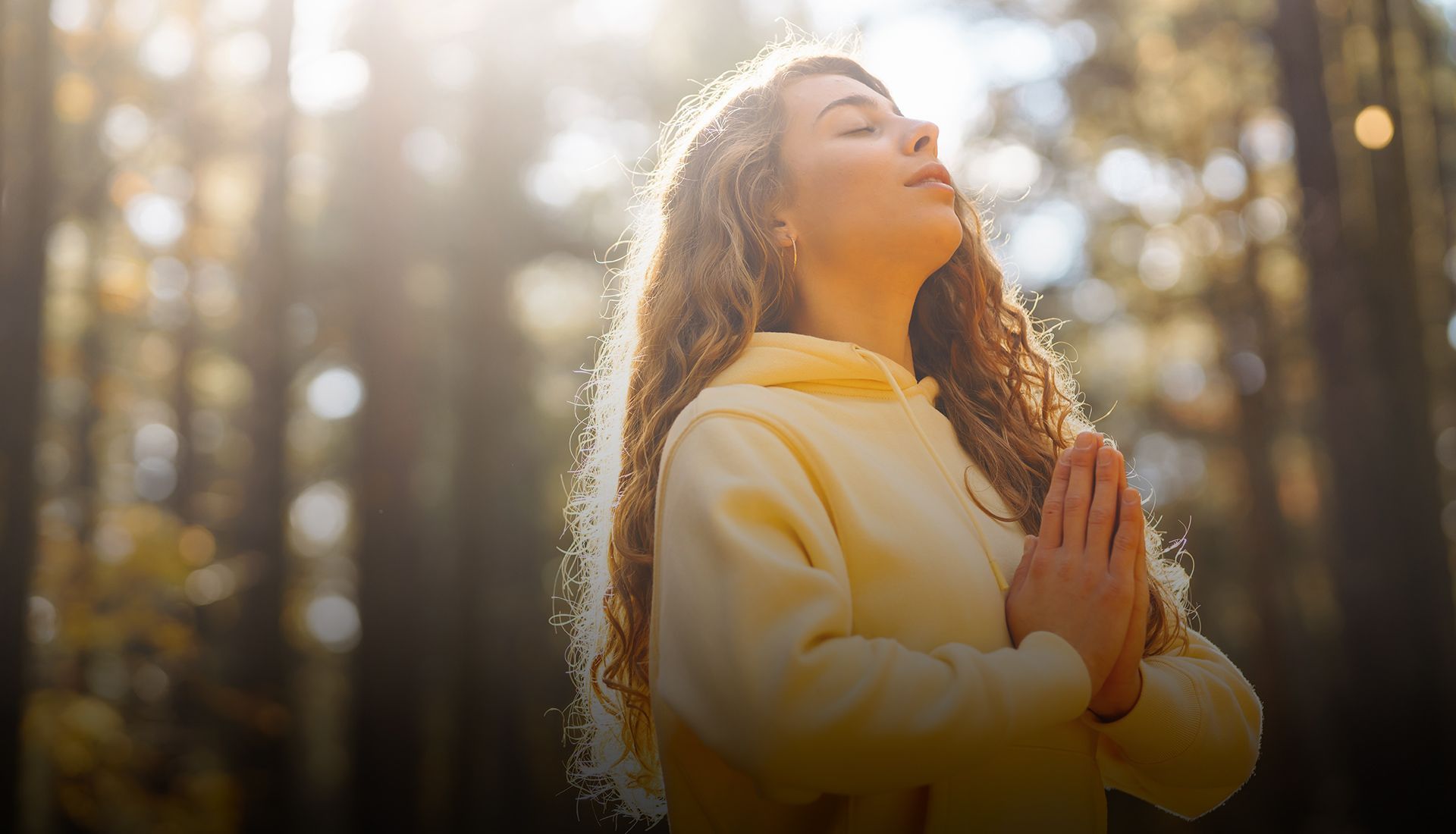 A woman is meditating in the woods with her eyes closed.