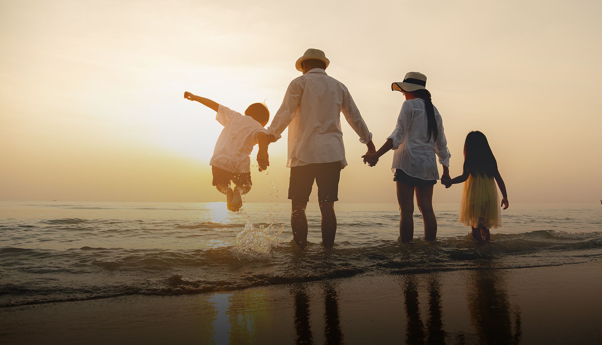 A family is standing on the beach holding hands at sunset.