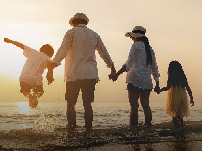 A family is holding hands on the beach at sunset.