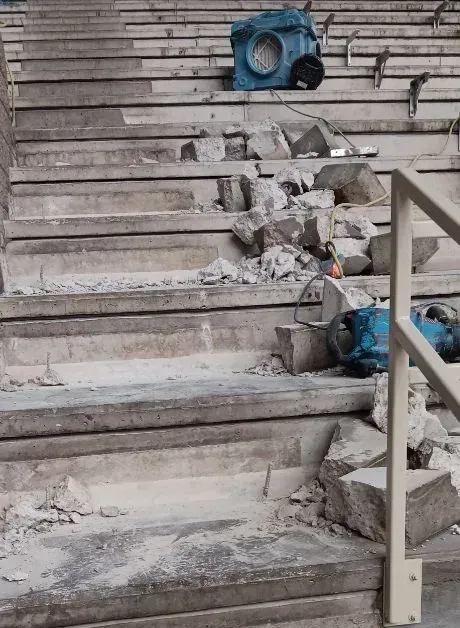 Stone steps undergoing construction or demolition, covered in concrete rubble with two blue power tools resting on them.