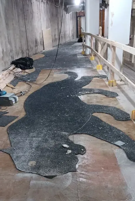 A dark mosaic floor inlay of a large cat, like a panther, being installed in an unfinished hallway with wooden railings.