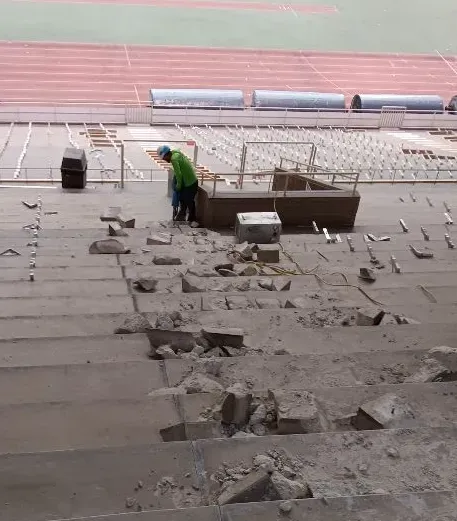 A construction worker in a green shirt removes damaged concrete seating at an outdoor stadium.