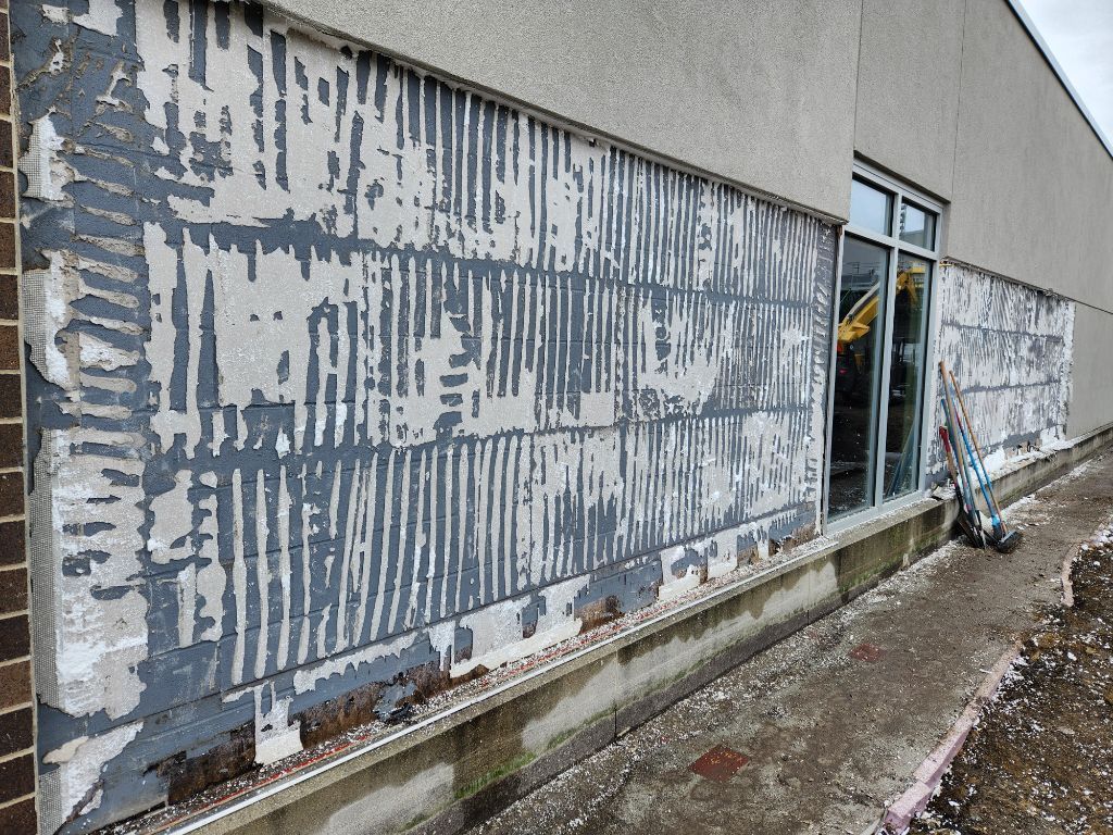 Exterior wall with peeling gray paint and a window near a wet concrete walkway