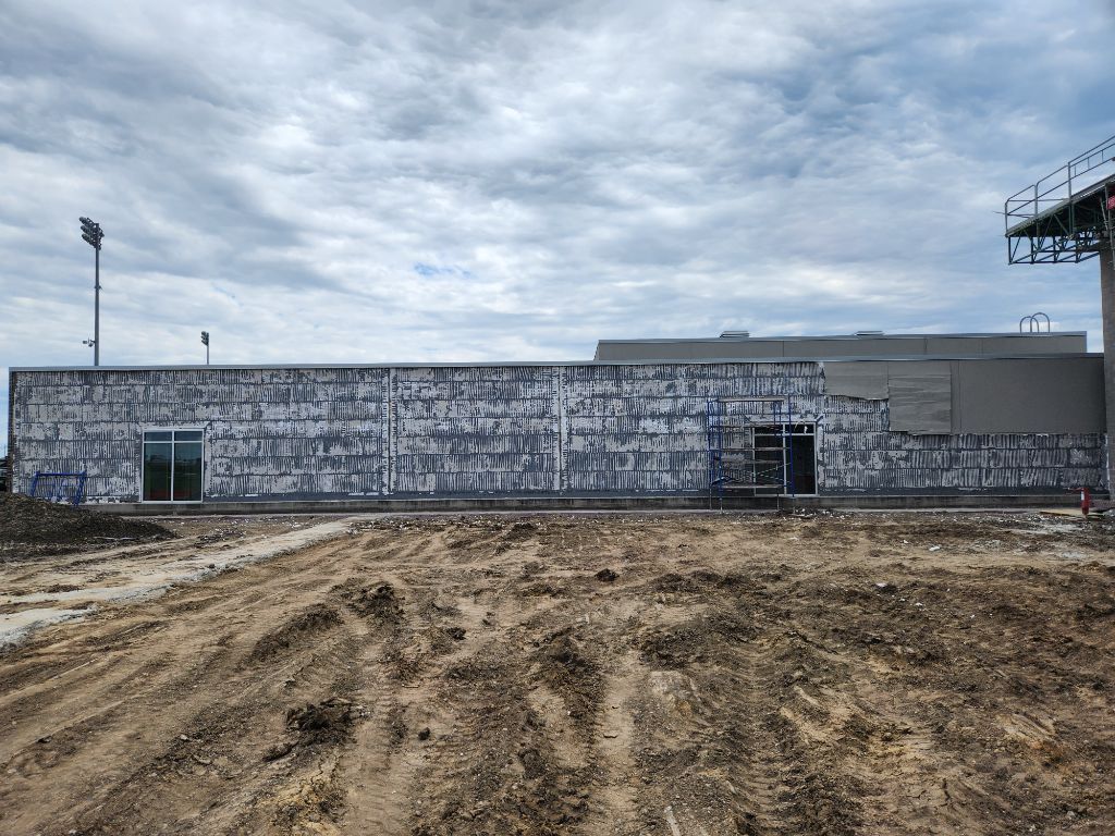 Bare dirt lot in front of a weathered gray industrial building under an overcast sky