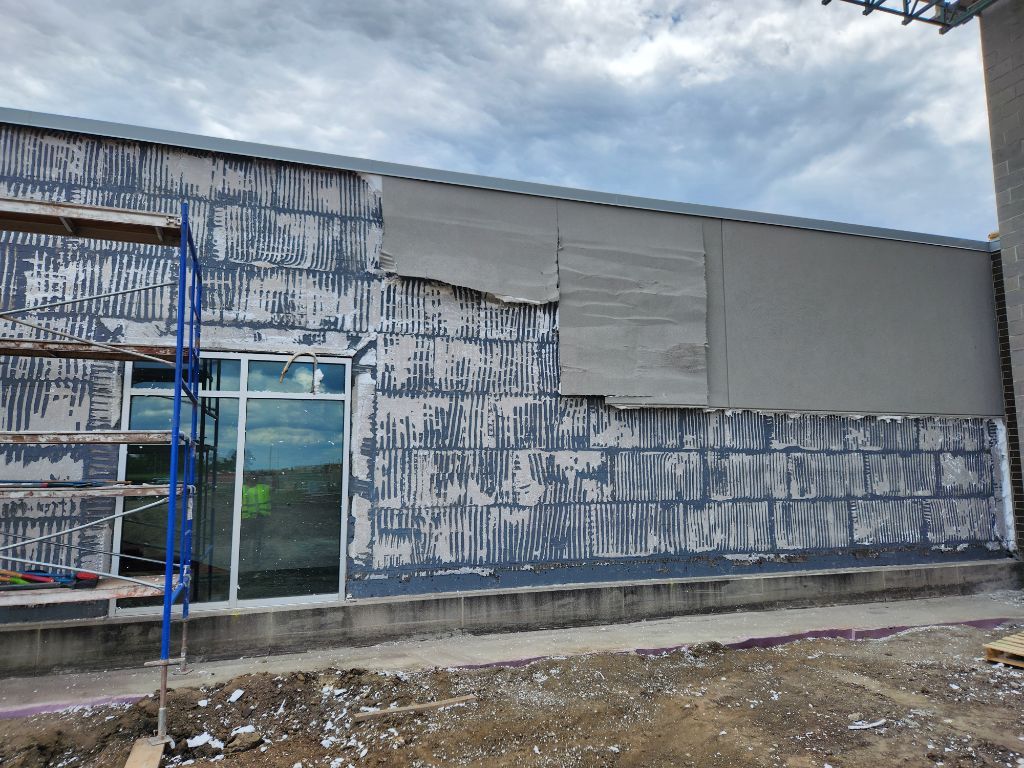 Weathered storefront with peeling blue paint, glass door, and unfinished gray siding under a cloudy sky