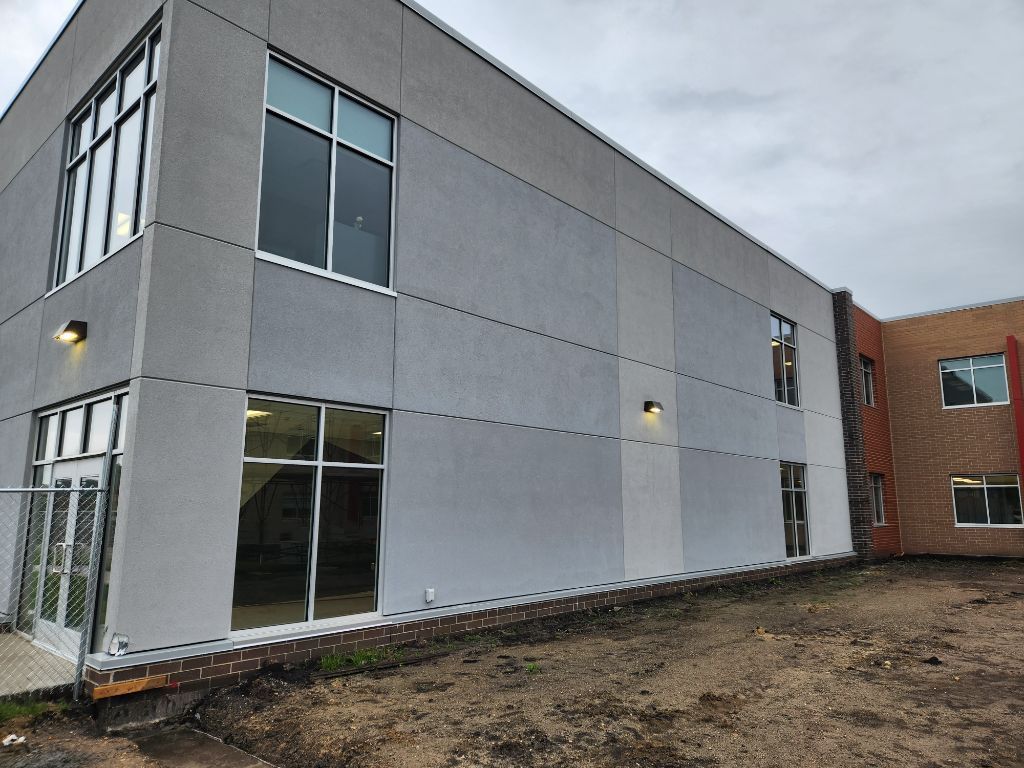 Modern gray building exterior with large windows and a red-brick section under a cloudy sky
