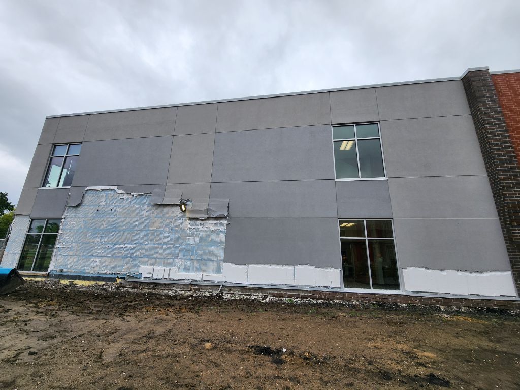 Gray building exterior with patchy repaired siding and muddy ground in front