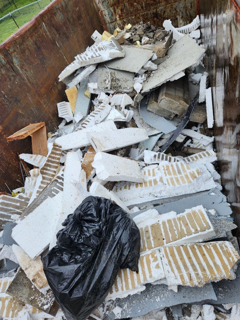 Dumpster filled with broken white debris and a black trash bag
