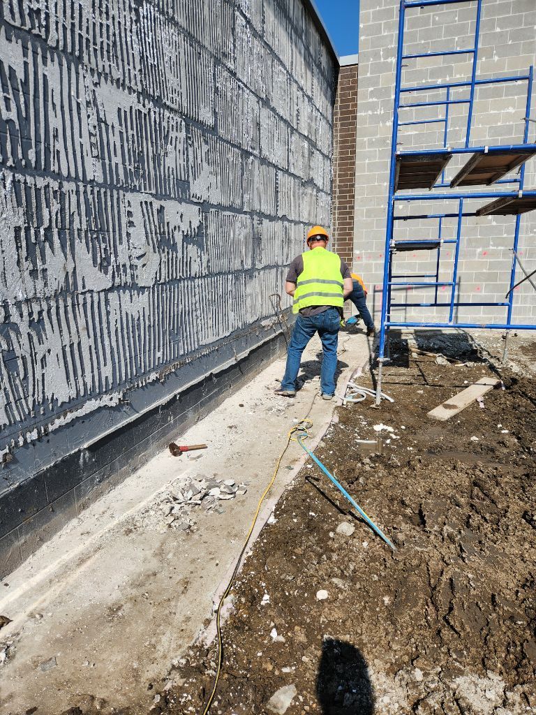 Worker in neon vest stands on a construction site beside a wall and scaffolding.