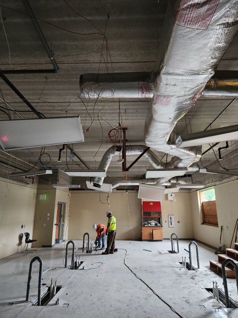 Workers inspecting a renovated office with exposed ductwork, hanging wires, and construction materials on the floor
