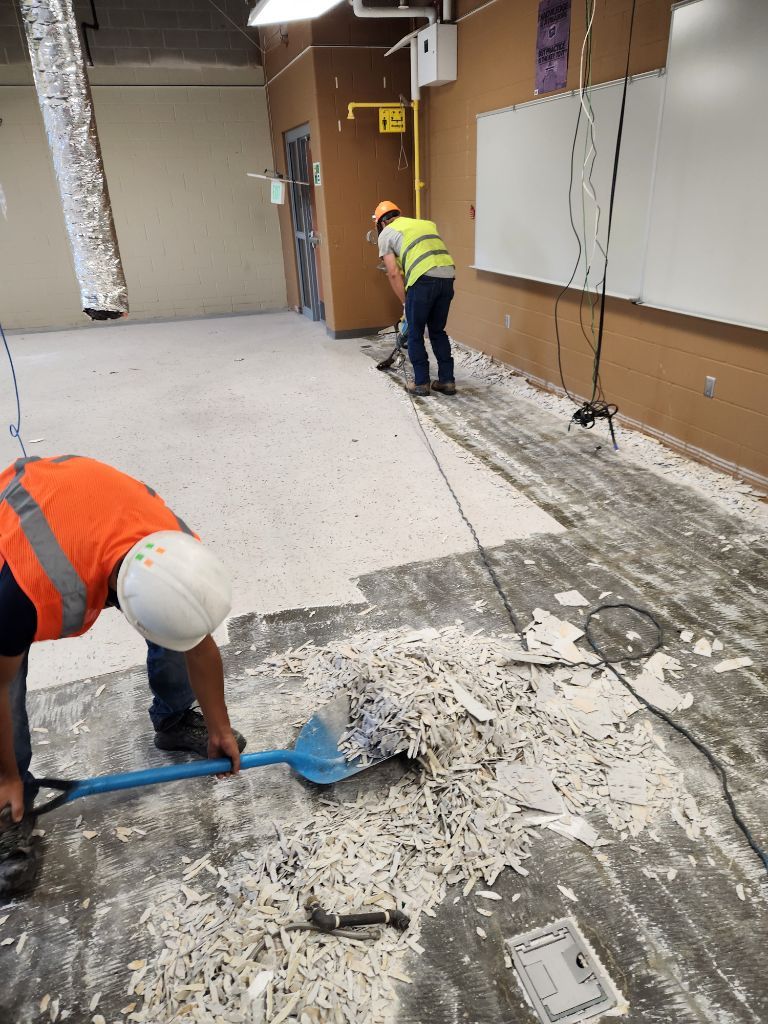 Construction workers repairing a damaged floor in an empty room, with concrete debris and tools.