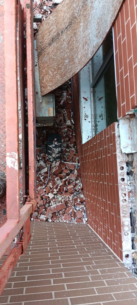 Rubble blocking a narrow brick walkway beside a damaged building wall and broken window