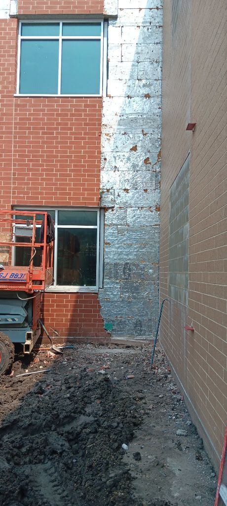 Narrow construction gap between brick buildings, with scaffolding and rubble on the ground.