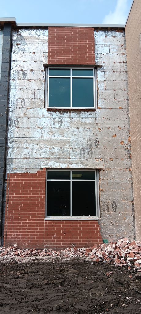 Partially demolished brick building facade with two windows and rubble in front