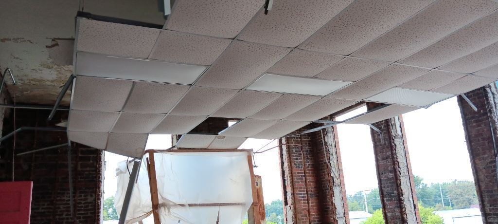 Partially unfinished ceiling with exposed panels and brick columns inside an open building under construction