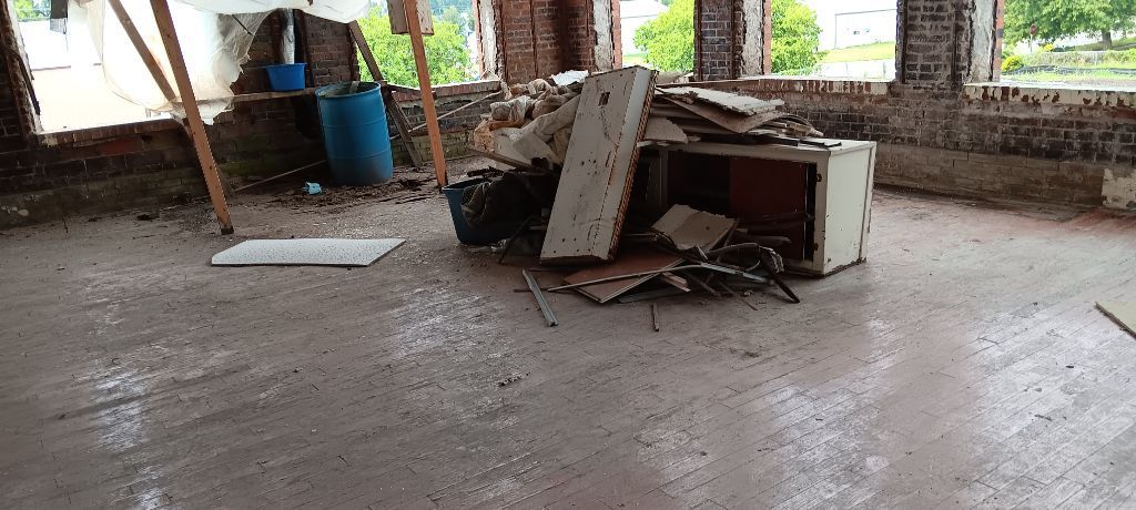 Damaged overturned cabinet and debris scattered across a dusty unfinished room with exposed brick walls