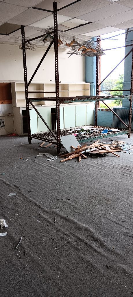 Damaged office with collapsed ceiling, scattered debris, and exposed framing near windows.
