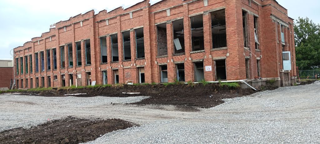 Abandoned red-brick industrial building with broken windows and gravel foreground