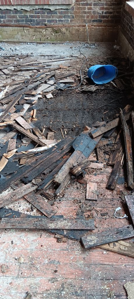 Damaged brick room with scattered debris and a tipped blue bucket on the floor