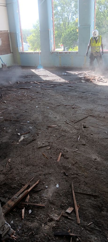 Unfinished room with dirt floor, open windows, and a worker standing near the right wall
