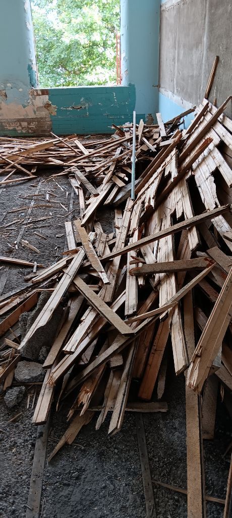 Pile of wooden planks and construction debris inside a partially renovated room with a window and blue wall.