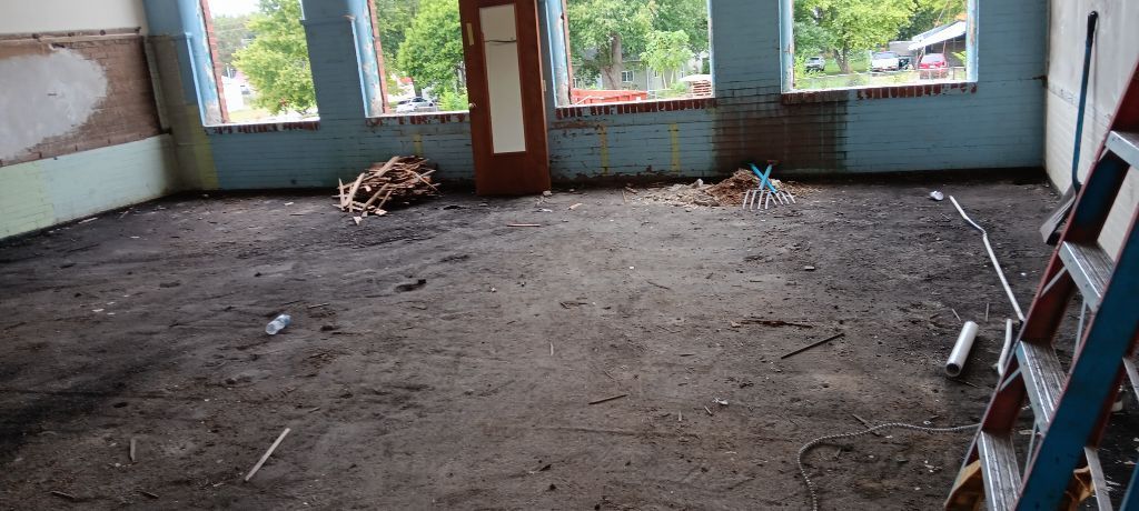 Empty room with bare dirt floor, large windows, and scattered construction debris.