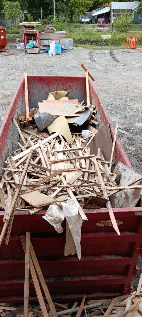 Red dumpster filled with broken wood and cardboard debris in a gravel yard