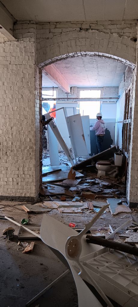Damaged interior with rubble, broken walls, and workers clearing debris through an arched doorway.