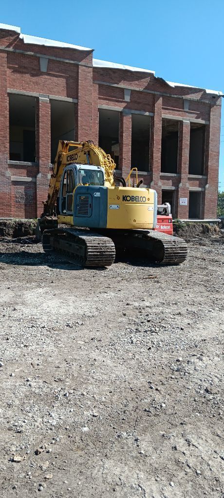 Yellow excavator parked on gravel in front of a brick building under construction