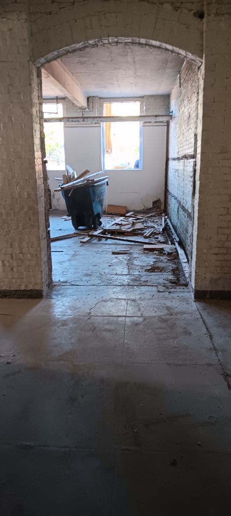 Abandoned hallway in a damaged building, with debris on the floor and a bright window at the end.