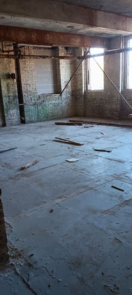 Abandoned unfinished room with concrete floor, exposed brick walls, and scattered debris near a window.