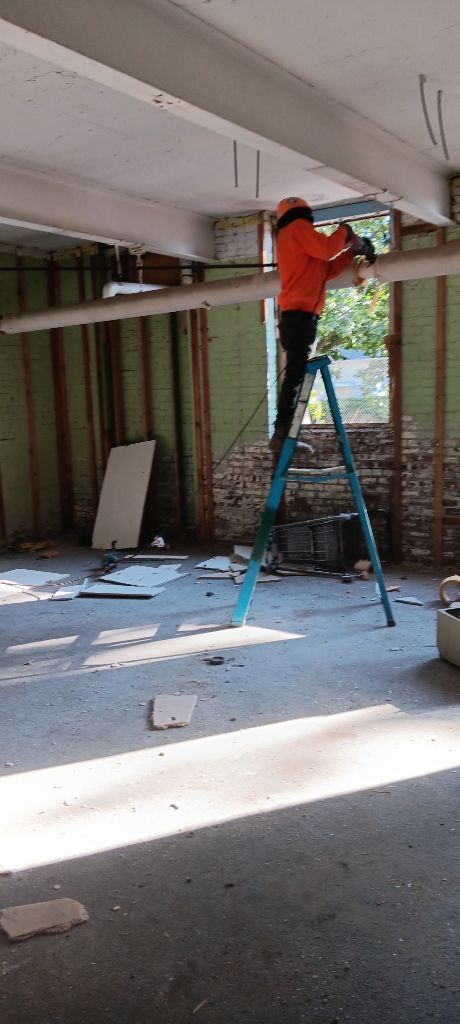 Worker in orange jacket standing on a ladder, fixing the ceiling in a renovation site.