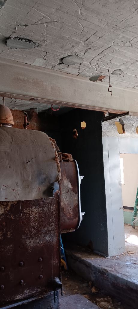 Dilapidated interior with cracked ceiling, rusted machinery, and a doorway into a dim room