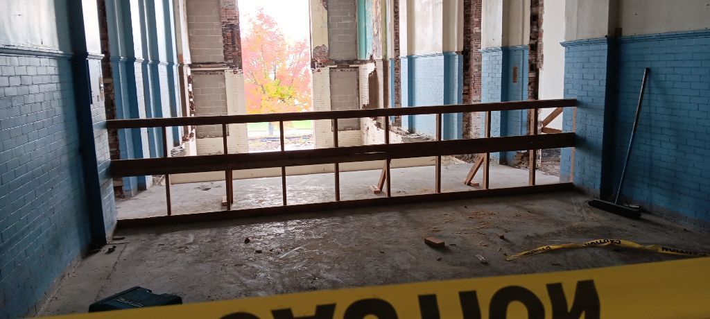 Wooden barricade blocking a doorway, with caution tape and a bright outdoor view beyond