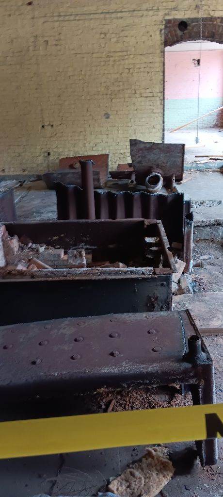 Abandoned room with scattered debris, rusted metal equipment, and a broken doorway opening to daylight