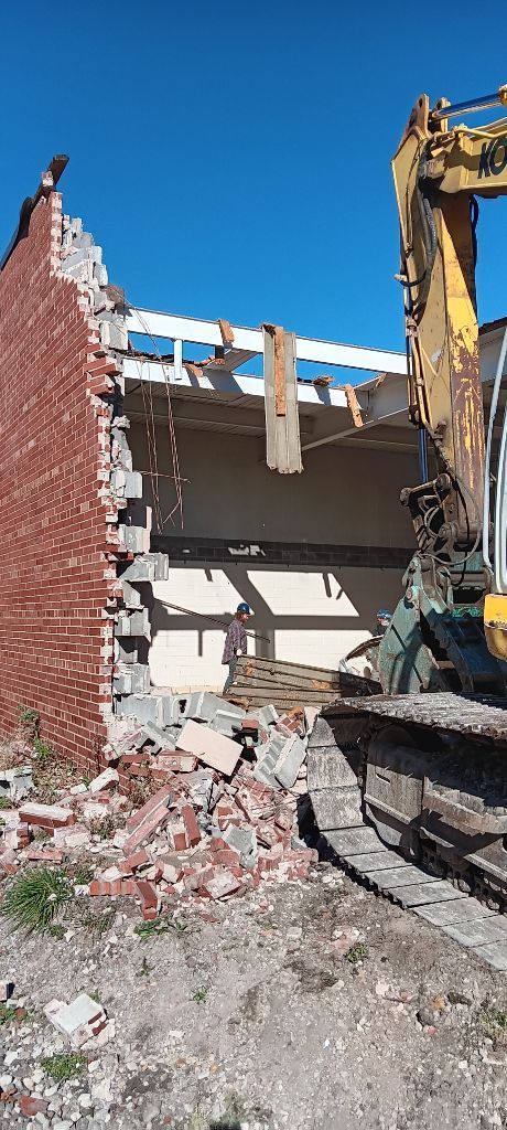Excavator demolishing a damaged brick wall at a construction site