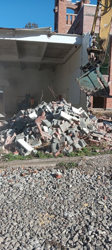 Collapsed concrete wall with rubble piled beside a gravel lot under a clear blue sky