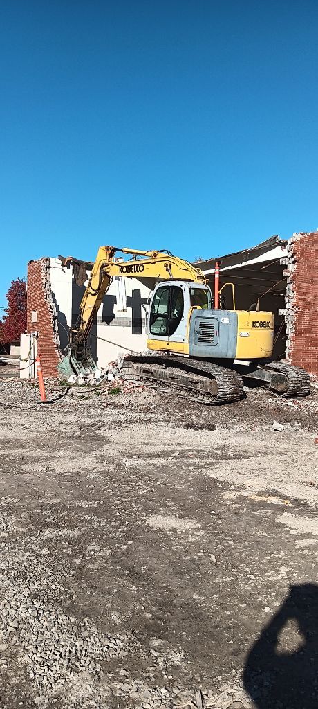 Construction equipment near a damaged brick building under a bright blue sky