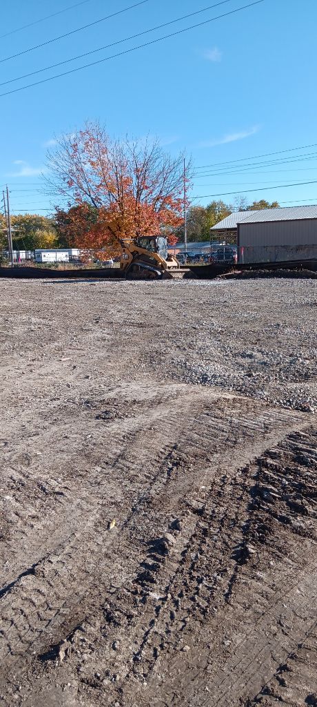 Gravel lot with a red-leaved tree and buildings under a clear blue sky