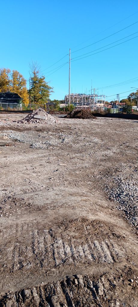 Gravel construction site with dirt mound, power lines, and a blue sky