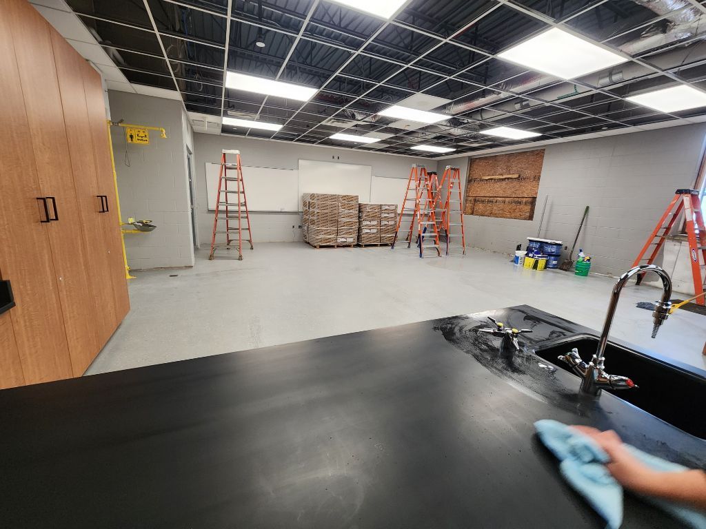 Empty office space under renovation with ladders, stacked materials, and a person cleaning the floor