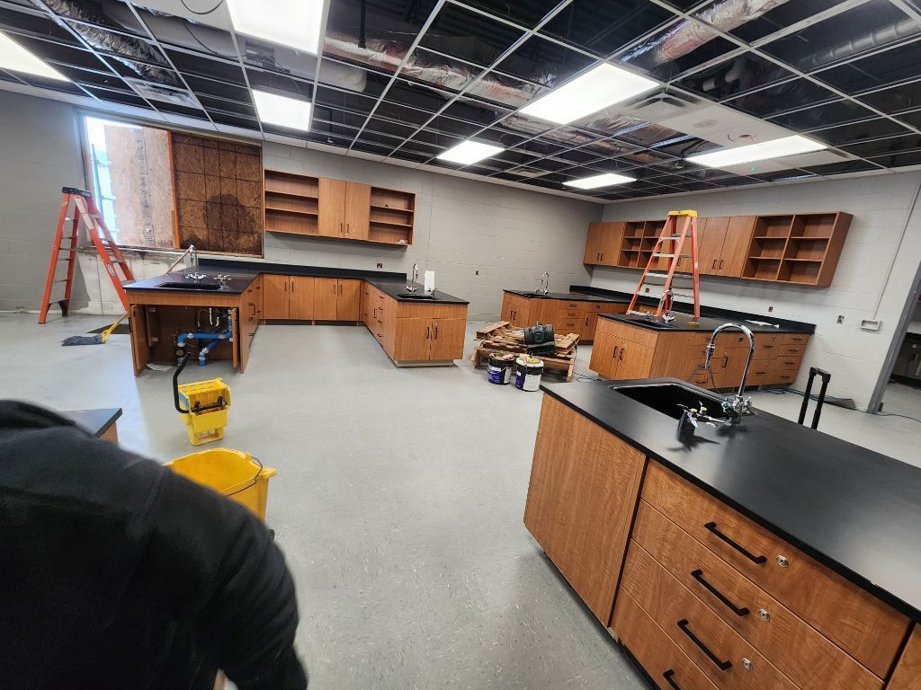 Science lab with cabinets, countertops, sinks, ladders, and yellow floor-cleaning machines in a large room