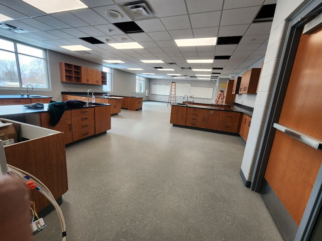 Empty science lab classroom with wooden cabinets, sinks, and large windows under fluorescent ceiling lights