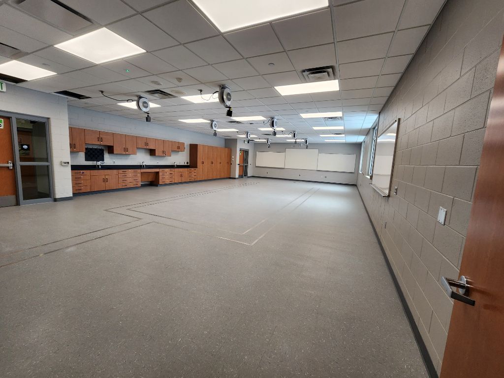 Empty classroom or office space with carpeted floor, desks, cabinets, and fluorescent ceiling lights