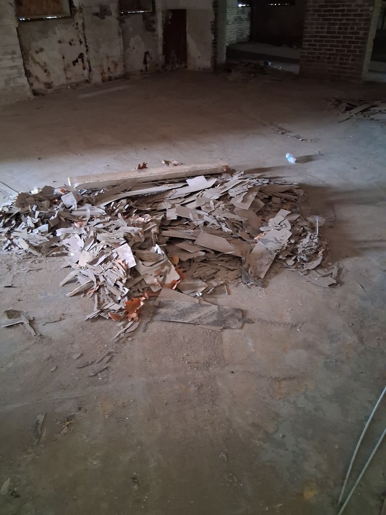 Pile of broken plaster and debris on a dusty floor in an empty, unfinished room.