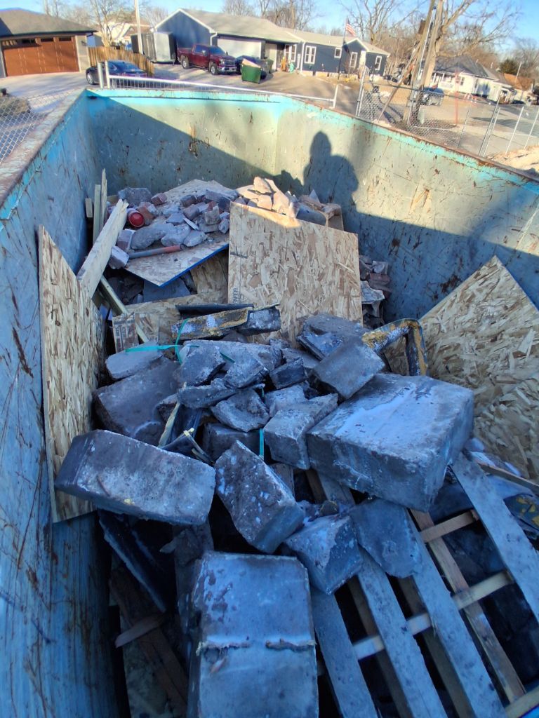 Dumpster filled with broken concrete blocks and debris at a construction site in winter sunlight