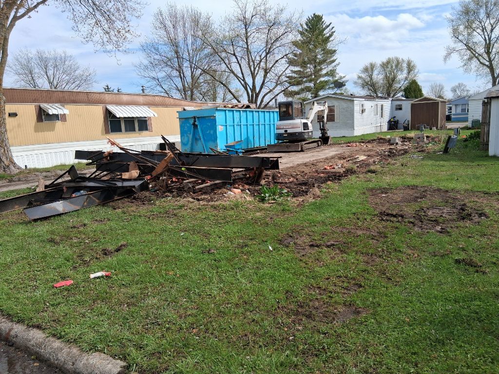 Burned debris in a muddy yard with a blue dumpster and white trailers in the background